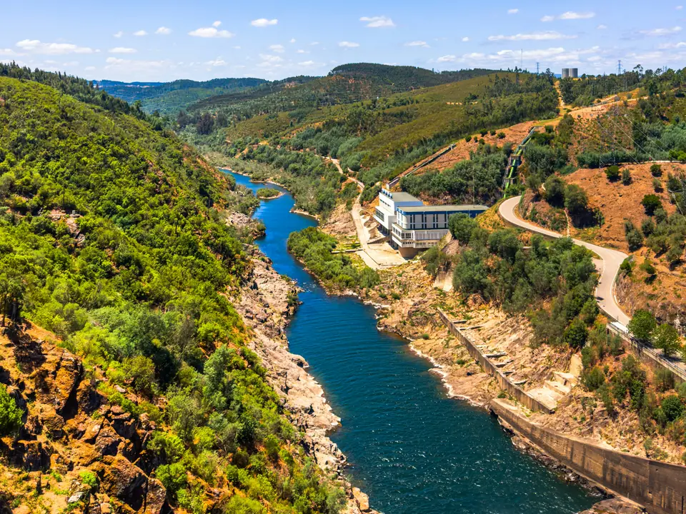 A blue river winding through a steep wooded valley past a hydroelectric building, photographed near Tomar in the Zêzere valley